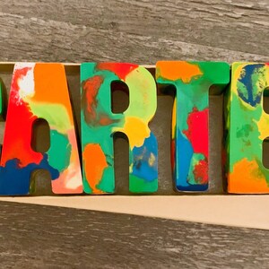 May include: Colorful, multi-colored, crayon letters spelling out the name "CARTER". The letters are in a box with a white label that says "CARTER" in a heart.