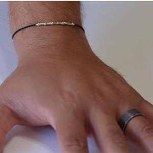 May include: A black string bracelet with silver beads and a silver ring on a finger.