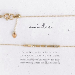 May include: Gold necklace with a heart charm and a bar charm with the word "auntie" spelled out in international morse code. The necklace is made with 14k gold-filled and 925 silver. It is water-friendly and made with love in Houston.