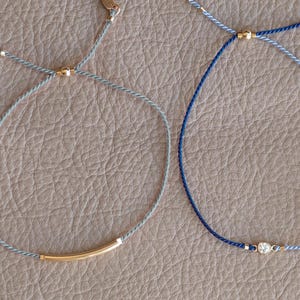 May include: Two adjustable bracelets with gold accents. One bracelet is gray with a gold bar and the other is blue with a gold bead and a small clear stone.