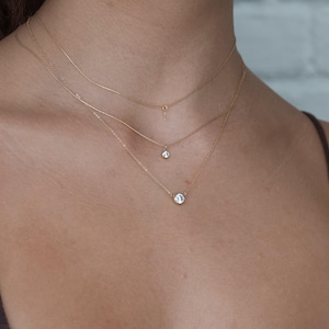 May include: Three delicate gold necklaces with small diamond accents. The necklaces are layered on a person's neck, creating a stylish and elegant look.
