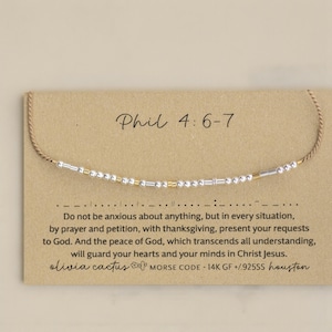 May include: A beaded bracelet with silver and gold-coloured beads is displayed on a brown card. The card has the text "Phil 4:6-7" and a quote about prayer. The brand name "olivia cactus" is also visible.