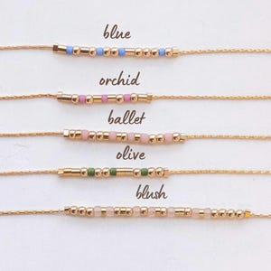 May include: Five gold chains with different colored beads, labeled "blue", "orchid", "ballet", "olive", and "blush".
