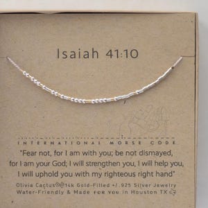 May include: A silver and gold beaded bracelet with the text "Isaiah 41:10" and the quote "Fear not, for I am with you; be not dismayed, for I am your God; I will strengthen you, I will help you, I will uphold you with my righteous right hand" on a brown card.