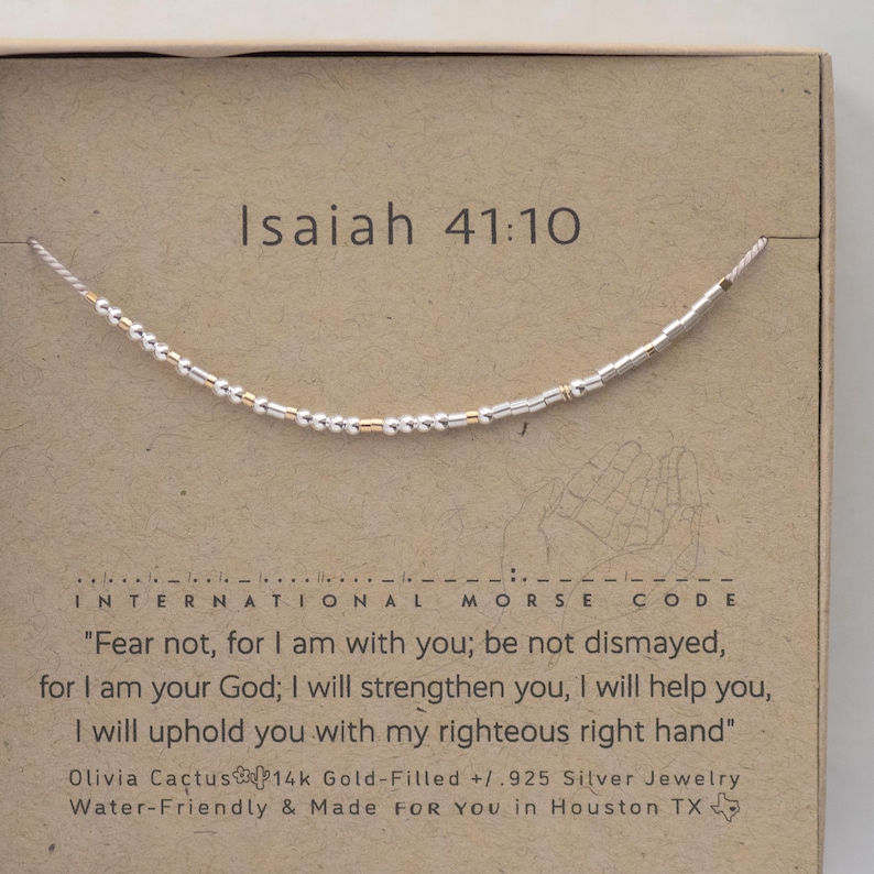May include: A silver and gold beaded bracelet with the text "Isaiah 41:10" and the quote "Fear not, for I am with you; be not dismayed, for I am your God; I will strengthen you, I will help you, I will uphold you with my righteous right hand" on a brown card.