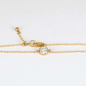 May include: A gold-toned chain bracelet featuring a single round, clear, faceted stone set in a bezel setting. The bracelet includes a delicate link chain, a lobster claw clasp, and an adjustable extension chain finished with a small gold-toned bead.
