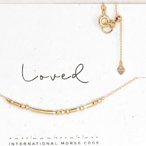 May include: A gold necklace with a delicate chain and a charm that says "loved" in international Morse code.