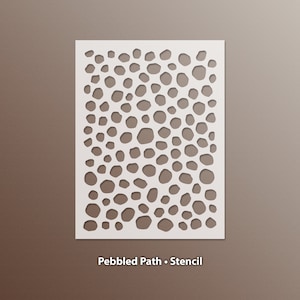 May include: A white stencil with a pattern of irregularly shaped holes, resembling pebbles. The stencil is rectangular and sits against a brown background. The text "Pebbled Path • Stencil" is at the bottom.