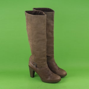 May include: A pair of brown leather knee-high boots with a block heel and a buckle detail on the shaft.
