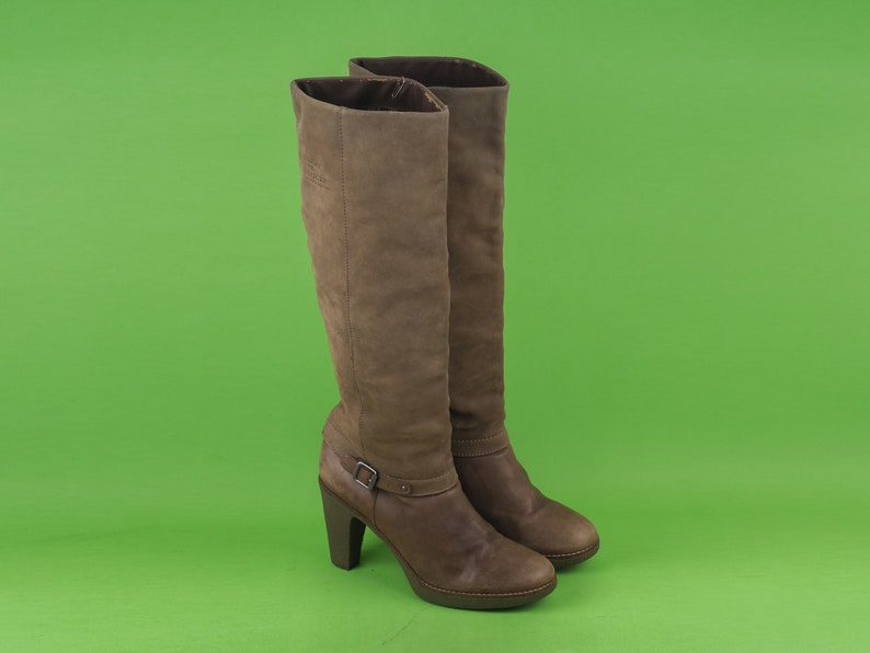 May include: A pair of brown leather knee-high boots with a block heel and a buckle detail on the shaft.