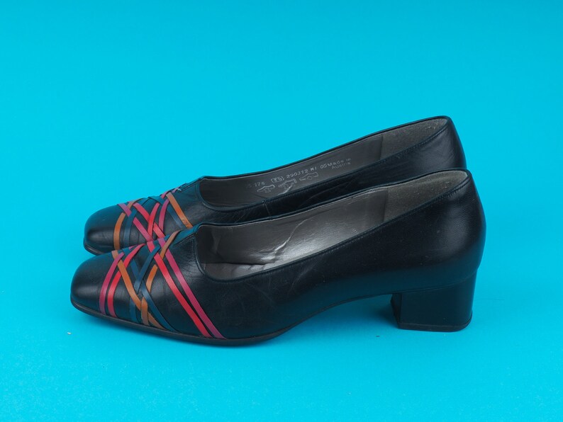 May include: Black leather low heeled shoes with a colorful woven design across the toe.