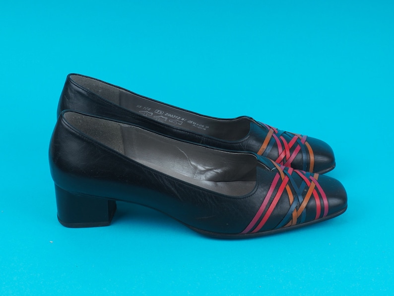 May include: A pair of black leather heeled shoes with a woven design in red, orange, and blue.