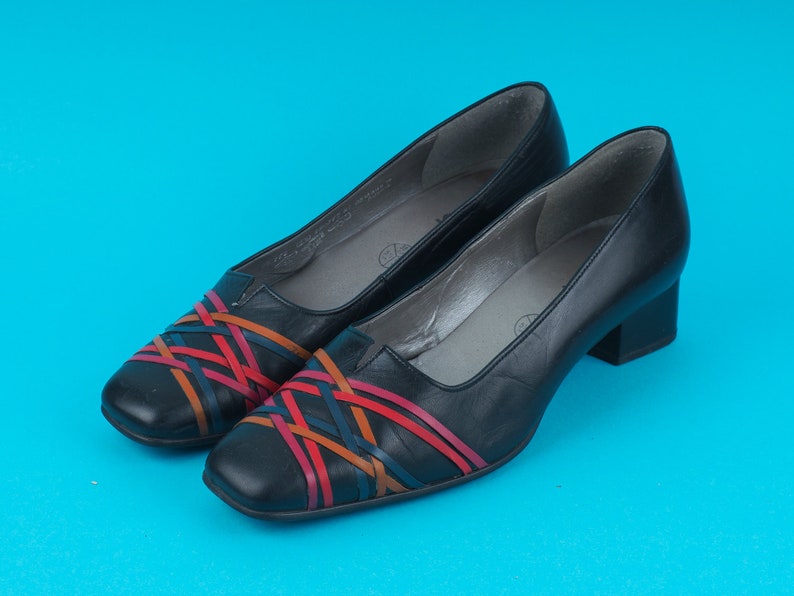 May include: A pair of black leather heeled shoes with a woven design in red, orange, and blue.