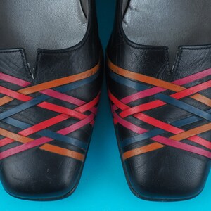 May include: A pair of black leather flats with a woven design in red, orange, and blue.