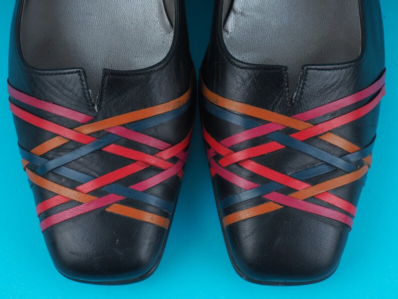 May include: A pair of black leather flats with a woven design in red, orange, and blue.