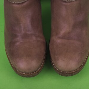 May include: A pair of brown leather boots with a rounded toe and a stitched seam around the edge.