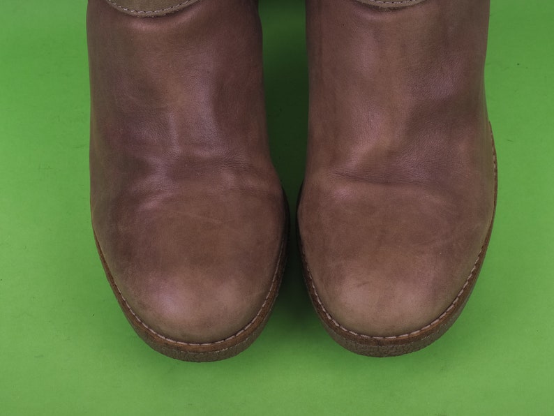 May include: A pair of brown leather boots with a rounded toe and a stitched seam around the edge.