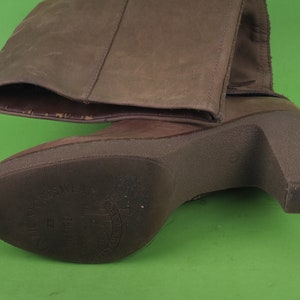 May include: Brown leather heeled boots with a zipper on the side and a brown sole. The sole has the text "Made in Italy" printed on it.