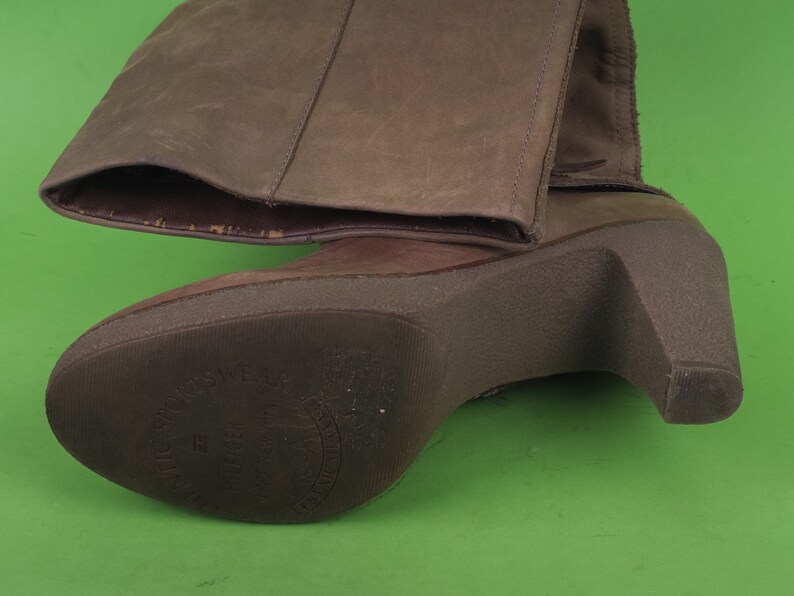 May include: Brown leather heeled boots with a zipper on the side and a brown sole. The sole has the text "Made in Italy" printed on it.