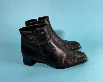 May include: A pair of black leather ankle boots with a square toe and a block heel. The boots have a zipper on the inside of each boot.