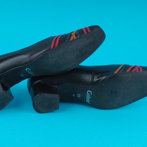 May include: A pair of black leather shoes with a low block heel. The shoes have a multi-colored striped design on the top and the brand name "Gabor" is printed on the sole.