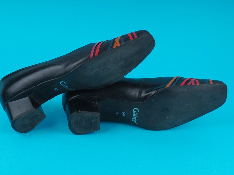 May include: A pair of black leather shoes with a low block heel. The shoes have a multi-colored striped design on the top and the brand name "Gabor" is printed on the sole.