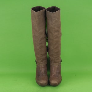 May include: A pair of brown leather knee-high boots with a buckle detail on the side.
