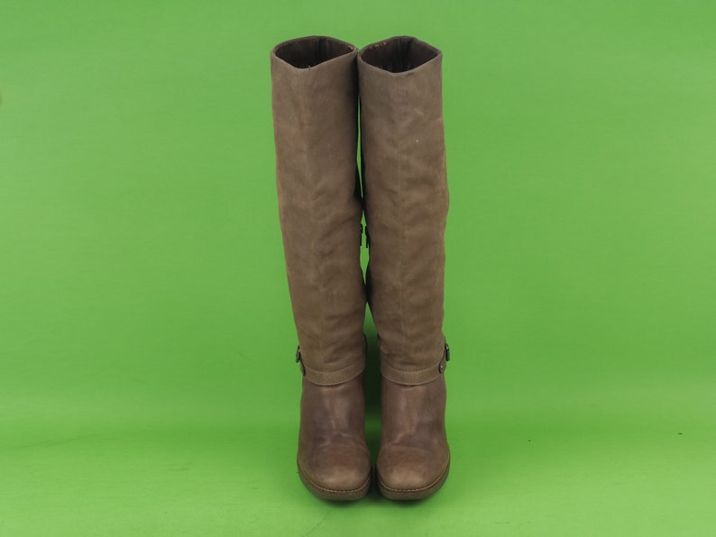 May include: A pair of brown leather knee-high boots with a buckle detail on the side.