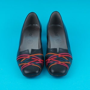 May include: A pair of black leather shoes with colorful woven straps. The shoes have a pointed toe and a low heel.