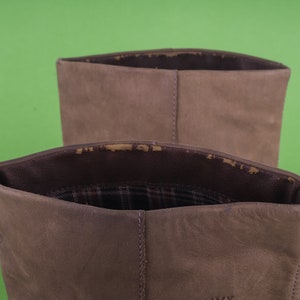 May include: Close-up of the top of two brown suede boots. The boots have a plaid lining.