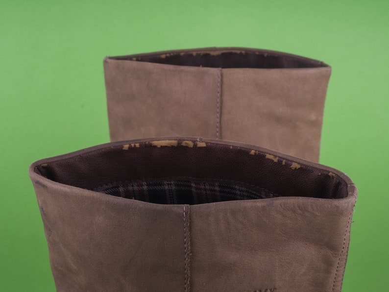 May include: Close-up of the top of two brown suede boots. The boots have a plaid lining.