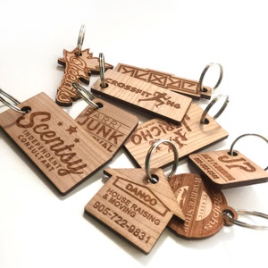 May include: A collection of wooden keyrings with various business logos and names, including "Scentsy", "Danco House Raising & Moving", "JP Jac's Plumbing", "Ralph's Classic Barber Shop", "CrossFit ENG", "Barri Junk", and "Richo Youth Services".