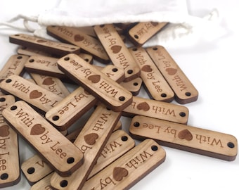 May include: A pile of wooden tags with the text "With Love by Lee" and a small heart symbol. The tags are light brown and have two holes for string or ribbon.