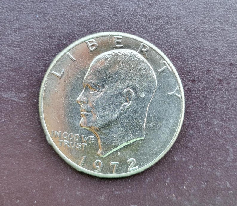 Op de afbeelding: Een zilveren Eisenhower-dollarmunt uit 1972. De munt toont een profiel van een man en de woorden "LIBERTY" en "IN GOD WE TRUST". Het jaartal "1972" is ook zichtbaar.