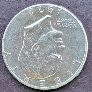 Op de afbeelding: Een zilveren 1972 Kennedy half dollar munt. De munt toont een profiel van John F. Kennedy en de woorden "LIBERTY" en "IN GOD WE TRUST". Het jaartal "1972" is zichtbaar aan de bovenkant.