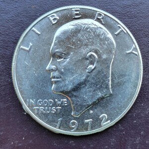 Op de afbeelding: Een zilveren Eisenhower dollar munt uit 1972. De munt toont een profiel van een man, het woord "LIBERTY" bovenaan, en "IN GOD WE TRUST" en de datum "1972" onderaan. De munt ligt op een donkere achtergrond.