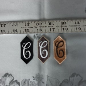 May include: Three embroidered iron-on patches in the shape of a hexagon. The patches are black, brown, and beige. Each patch has a white letter "C" in the centre.