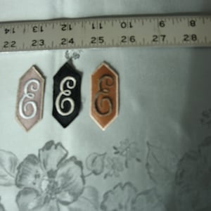 May include: Three embroidered fabric patches in the shape of a hexagon, each with the letter "E" in a different colour: white on pink, white on black, and brown on tan.