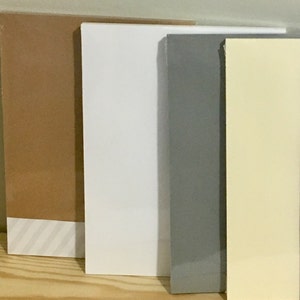 May include: Four different coloured pieces of cardstock, from left to right: brown, white, grey, and yellow.