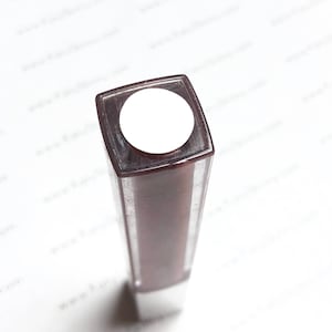 May include: A brown square-shaped bottle with a white lid. The bottle is partially filled with a dark liquid.