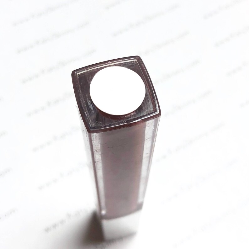 May include: A brown square-shaped bottle with a white lid. The bottle is partially filled with a dark liquid.