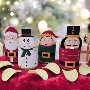 Könnte beinhalten: Vier Weihnachts-Snackbehälter mit Weihnachtsmann, Schneemann, Elf und Nussknacker. Die Behälter sind mit Kartoffelchips gefüllt und stehen auf einer roten, flauschigen Oberfläche.