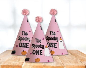 May include: Three pink party hats with black text that reads "The Spooky One" and a ghost and pumpkin design.