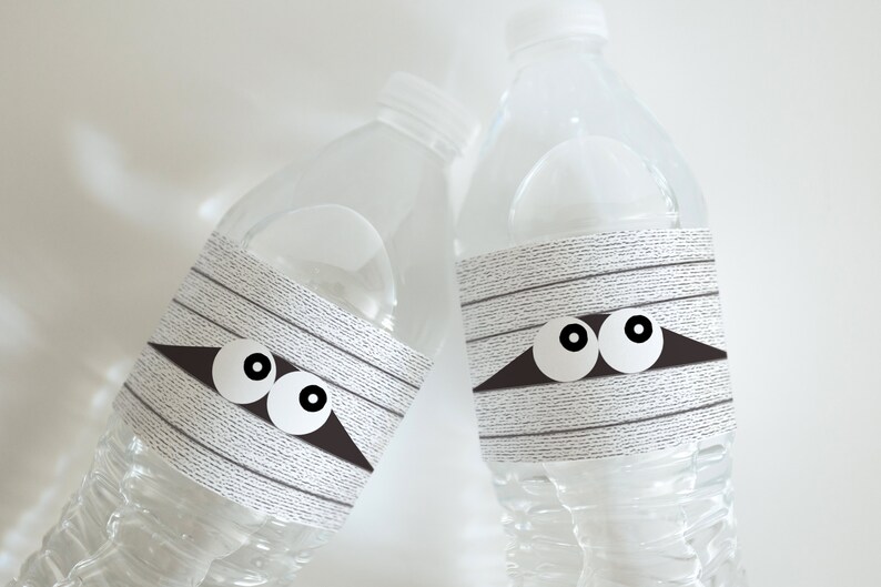May include: Two clear plastic water bottles with white and gray mummy-themed labels. The labels have black eyes and a black triangle shape.