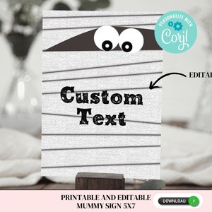 May include: Printable and editable mummy sign with a white background and black stripes. The sign features a mummy's face with two eyes peeking out from under a brown bandage. The text "Custom Text" is written in black on the sign.