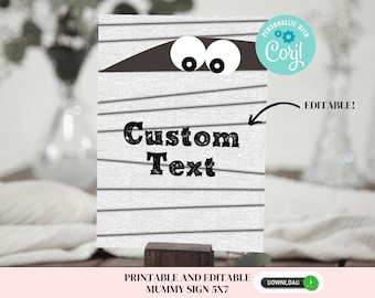 May include: Printable and editable mummy sign with a white background and black stripes. The sign features a mummy's face with two eyes peeking out from under a brown bandage. The text "Custom Text" is written in black on the sign.