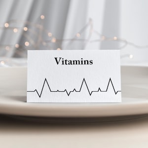May include: A white card with the word "Vitamins" printed in black text. A black line graph resembling a heartbeat is printed below the text.