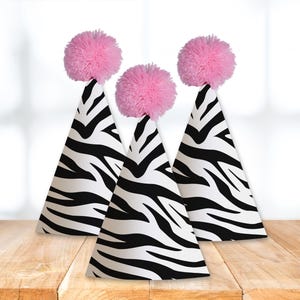 Peut inclure: Trois chapeaux de fête en papier à imprimé zèbre noir et blanc avec des pompons roses sur le dessus.