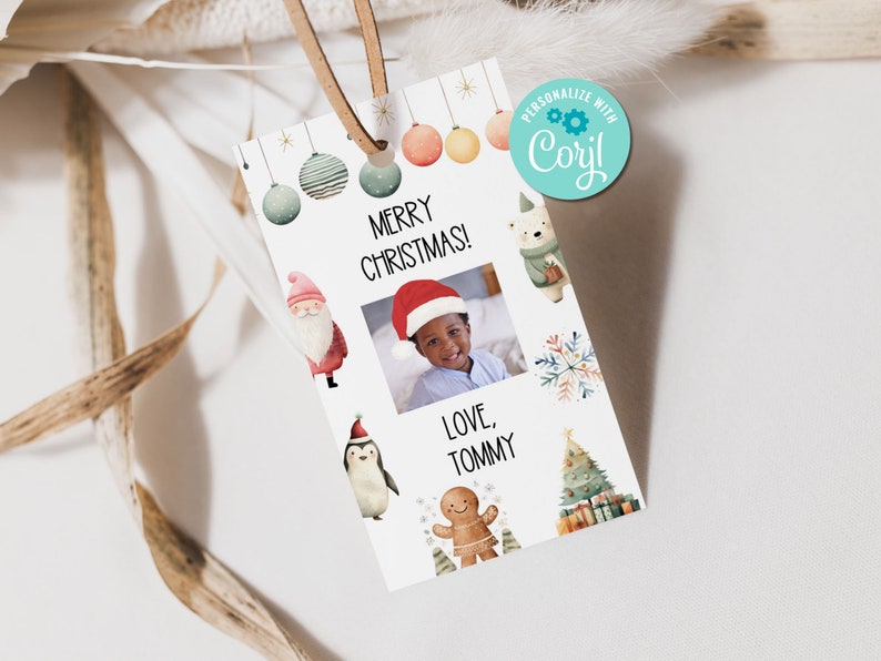 May include: A white Christmas gift tag with a brown leather string. The tag features the text "MERRY CHRISTMAS!" and a photo of a child wearing a Santa hat. Decorative illustrations include a Santa, penguin, and gingerbread man.