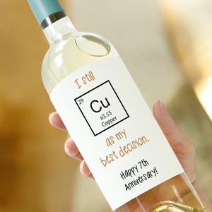 Può includere: Una bottiglia di vino bianco con un'etichetta che dice "I still Cu as my best decision. Happy 7th Anniversary!" L'etichetta presenta un simbolo di elemento chimico di rame.
